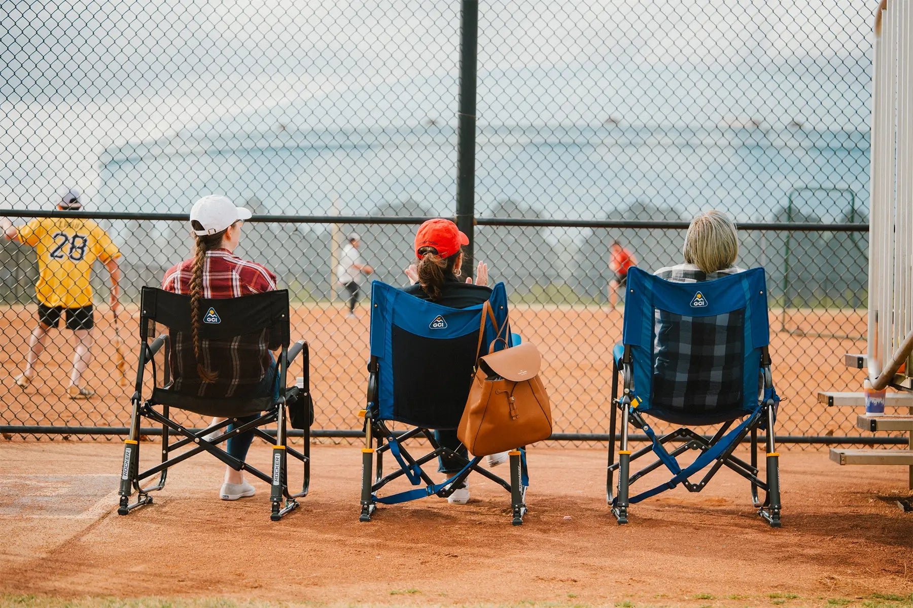 Three women cheering on a baseball game on the sidelines while sitting in different GCI chairs. 