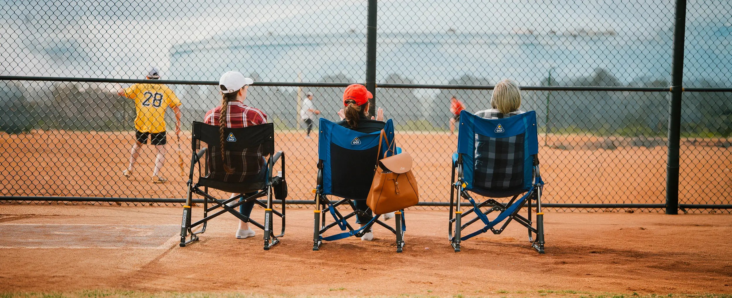 Three women cheering on a baseball game on the sidelines while sitting in different GCI chairs. 