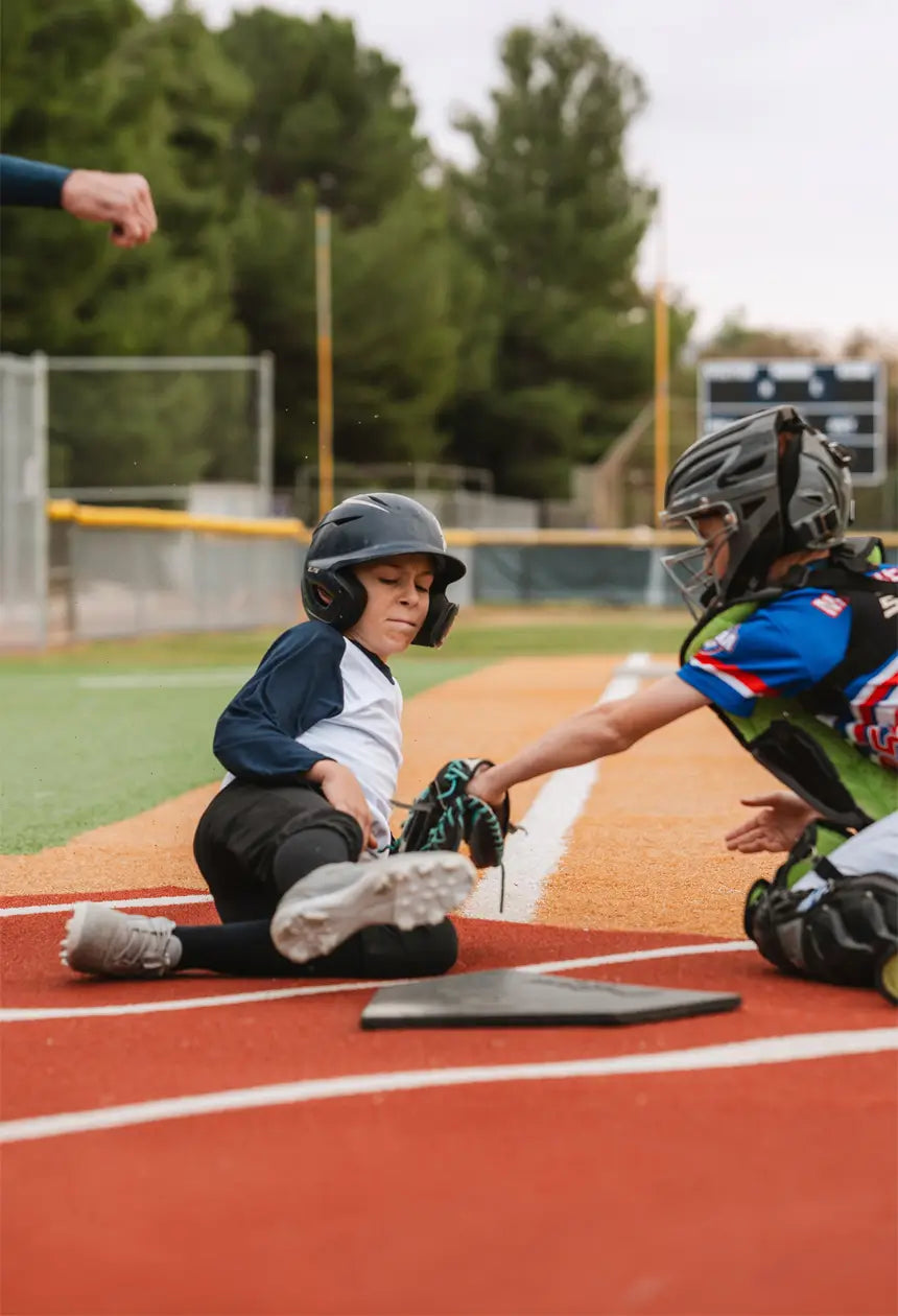 A young baseball player slides into home plate as the catcher reaches to tag them, both focused on the play.