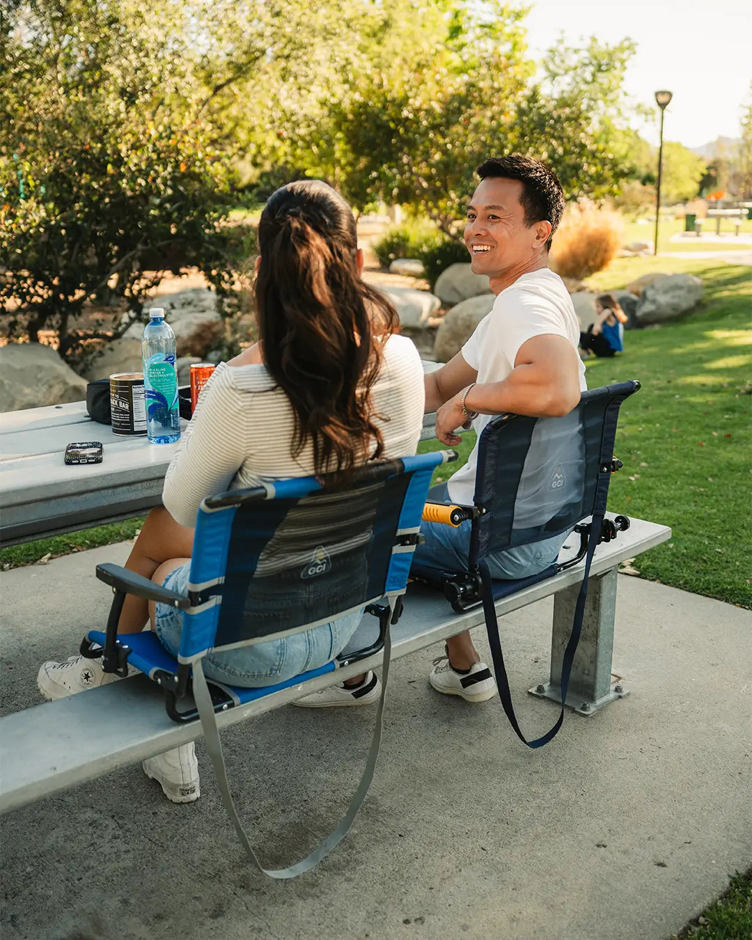 A couple sitting on a bench at the park in their GCI Outdoor stadium chairs. 