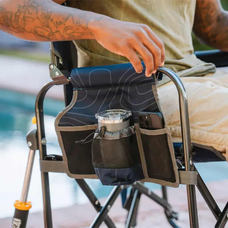 Close-up of a GCI Stowaway Rocker in Stealth Camo showing side storage pockets holding a cup and smartphone.