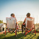 Two men sitting in a stowaway rocker baseball print next to a baseball field. 