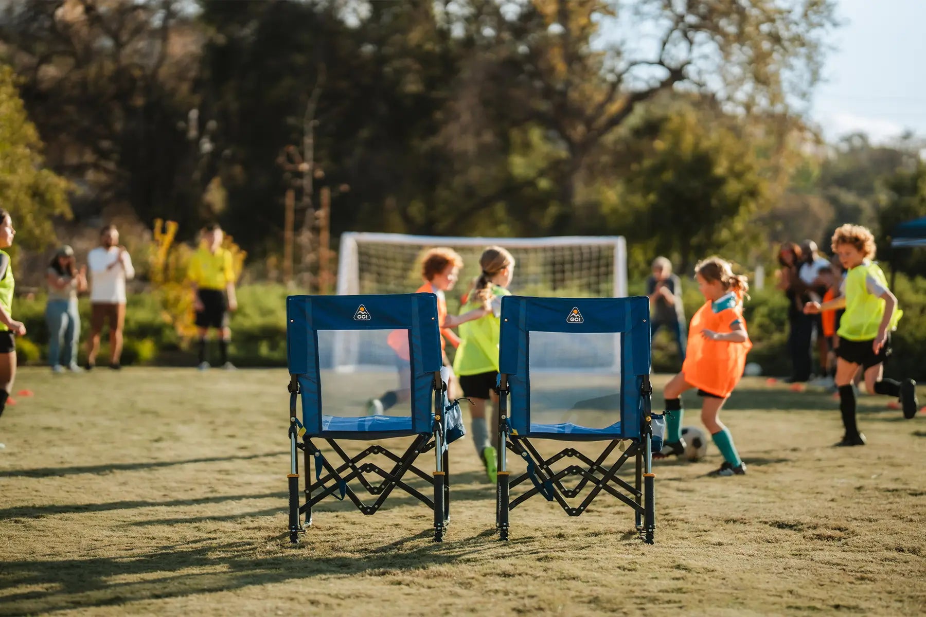 Two soft navy Stowaway Rockers positioned behind children who are playing soccer. 
