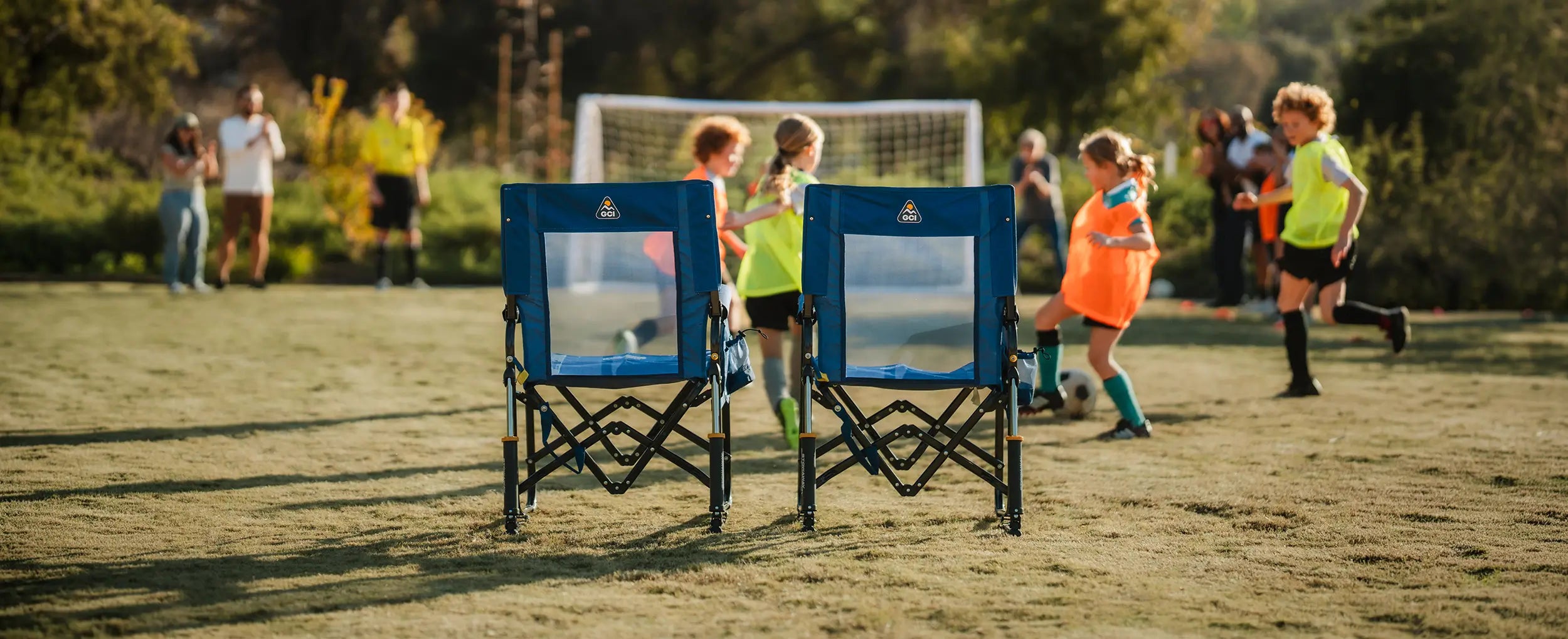 Two soft navy Stowaway Rockers positioned behind children who are playing soccer. 