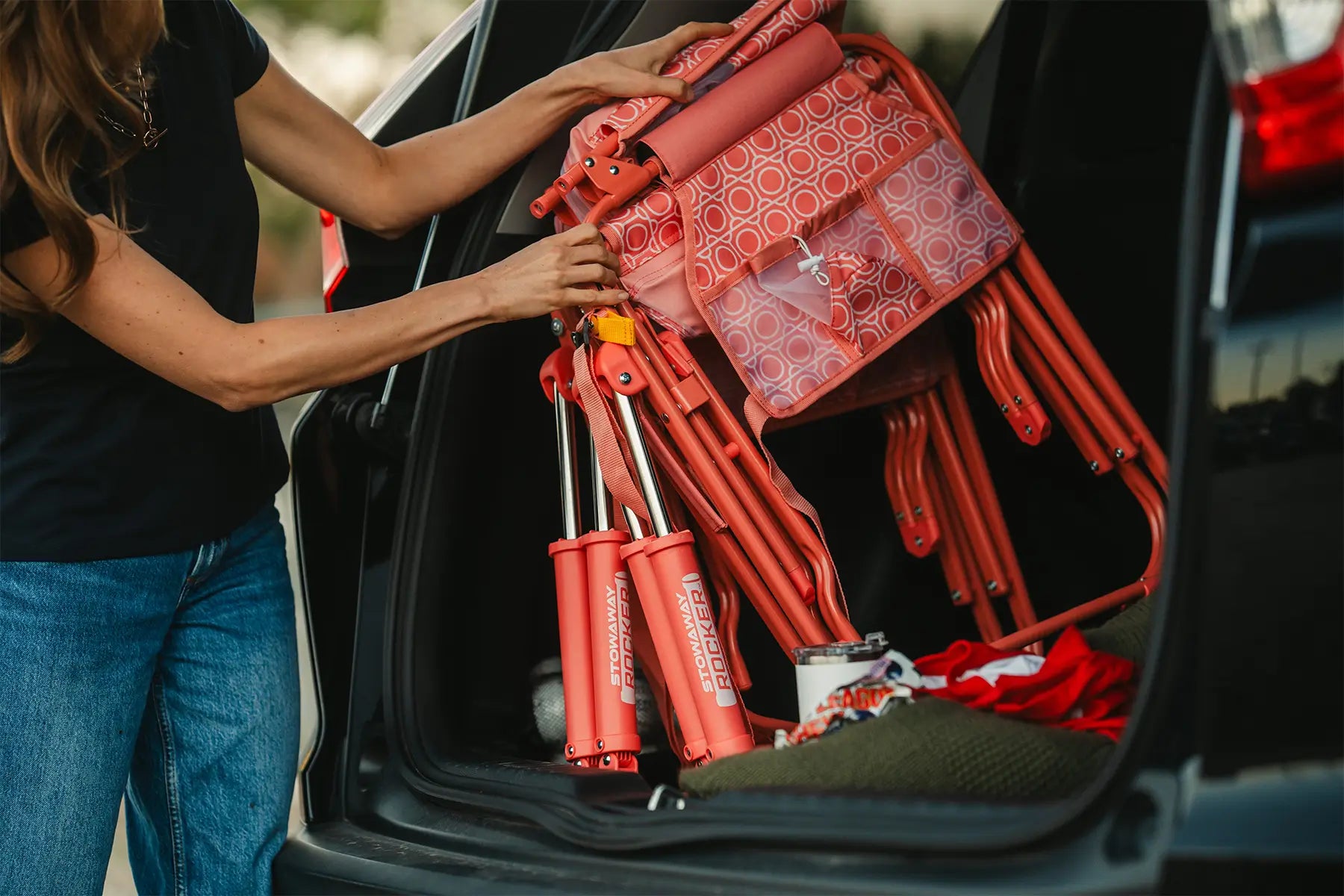 A woman pulling out a coral Stowaway Rocker from her trunk. 