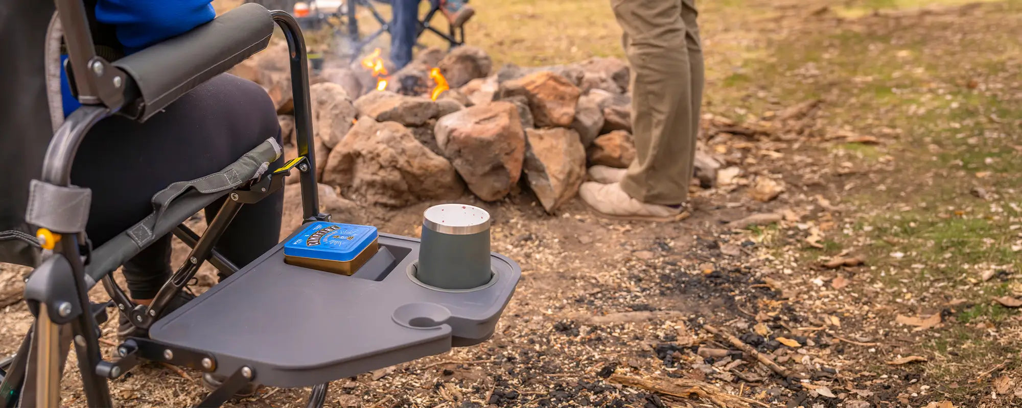 A tumbler and game resting on a Stowaway Rocker with Side Table at a campsite. 
