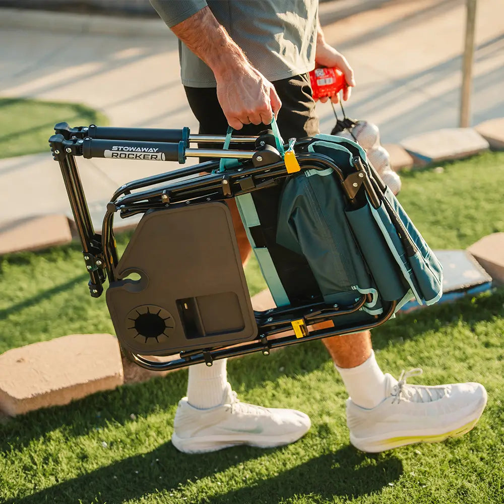 Person carrying the folded Teal Stowaway Rocker with Side Table by the handle for easy transport.