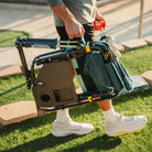 Person carrying the folded Teal Stowaway Rocker with Side Table by the handle for easy transport.