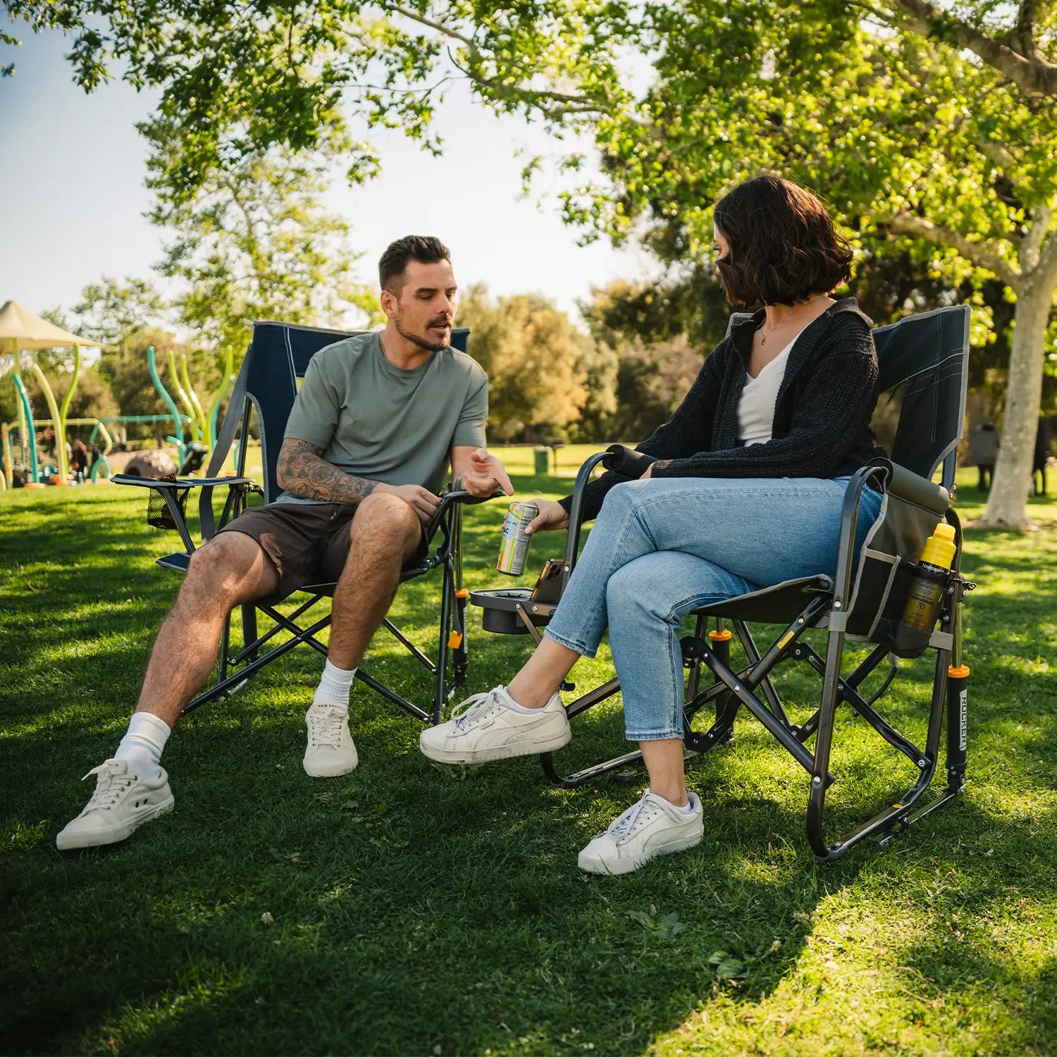 A couple sitting in their Comfort Pro Rocker and Stowaway with Side Table next to a playground. 