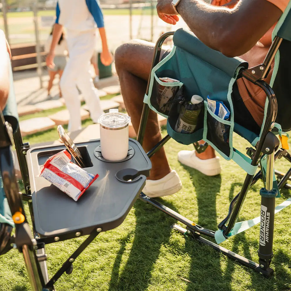 Close-up of the side table on the Teal Stowaway Rocker holding snacks and drinks during an outdoor event.
