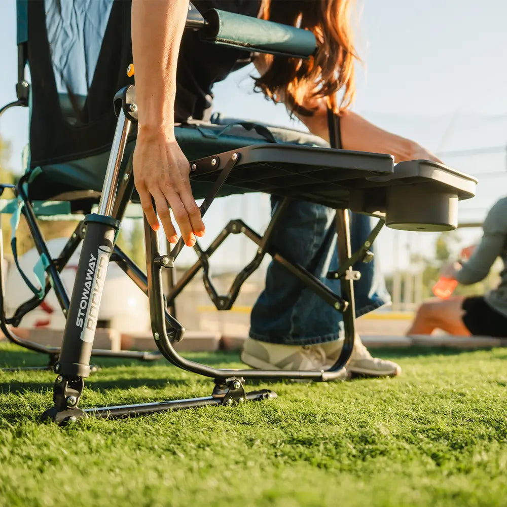 Person pulling out the side table on a Teal Stowaway Rocker while seated outdoors.