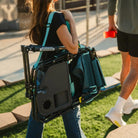 Person carrying the folded Teal Stowaway Rocker with Side Table over the shoulder while walking outdoors.