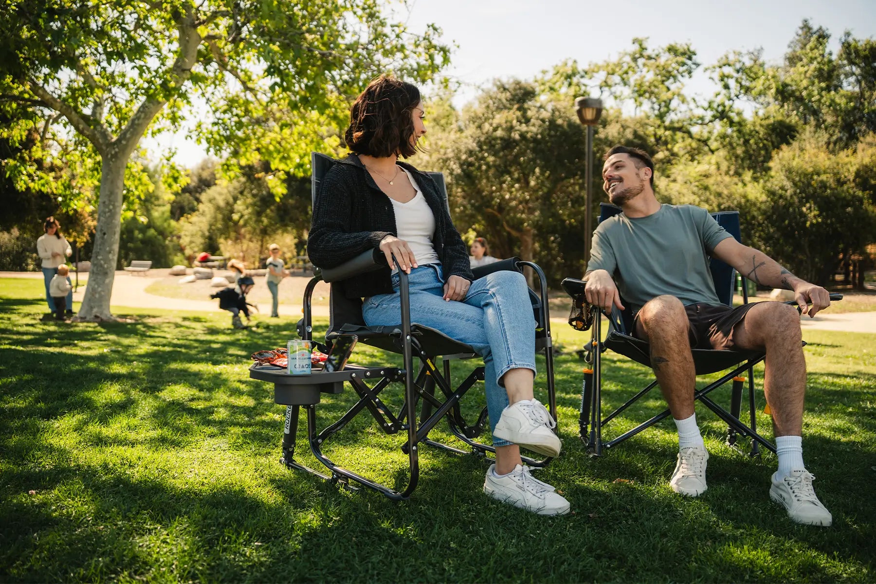 A couple sitting together in a Stowaway Rocker with Side Table and Comfort Pro Rocker at a park.