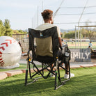 A man watching a baseball game while sitting in a stealth camo Stowaway Rocker. 