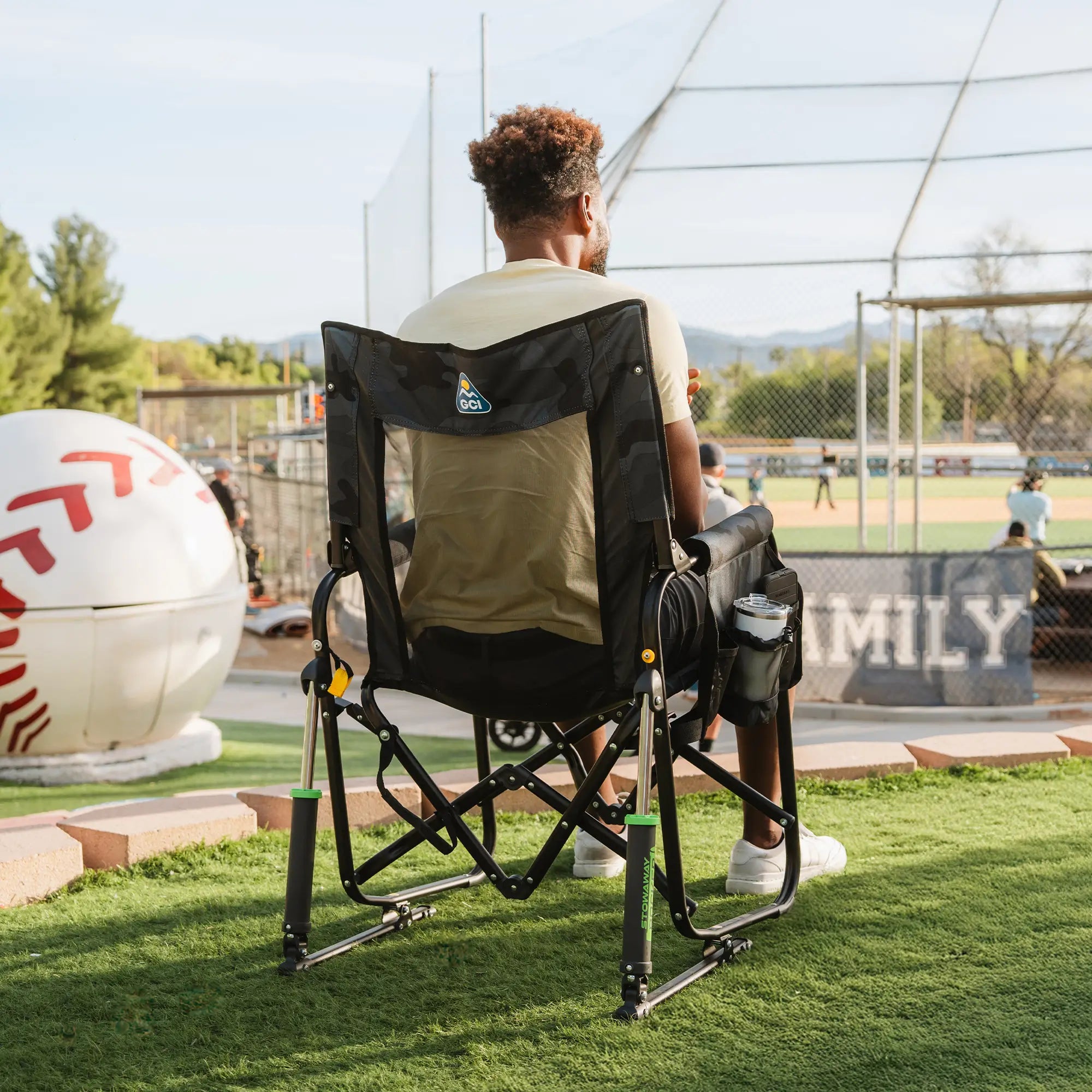 A man watching a baseball game while sitting in a stealth camo Stowaway Rocker. 