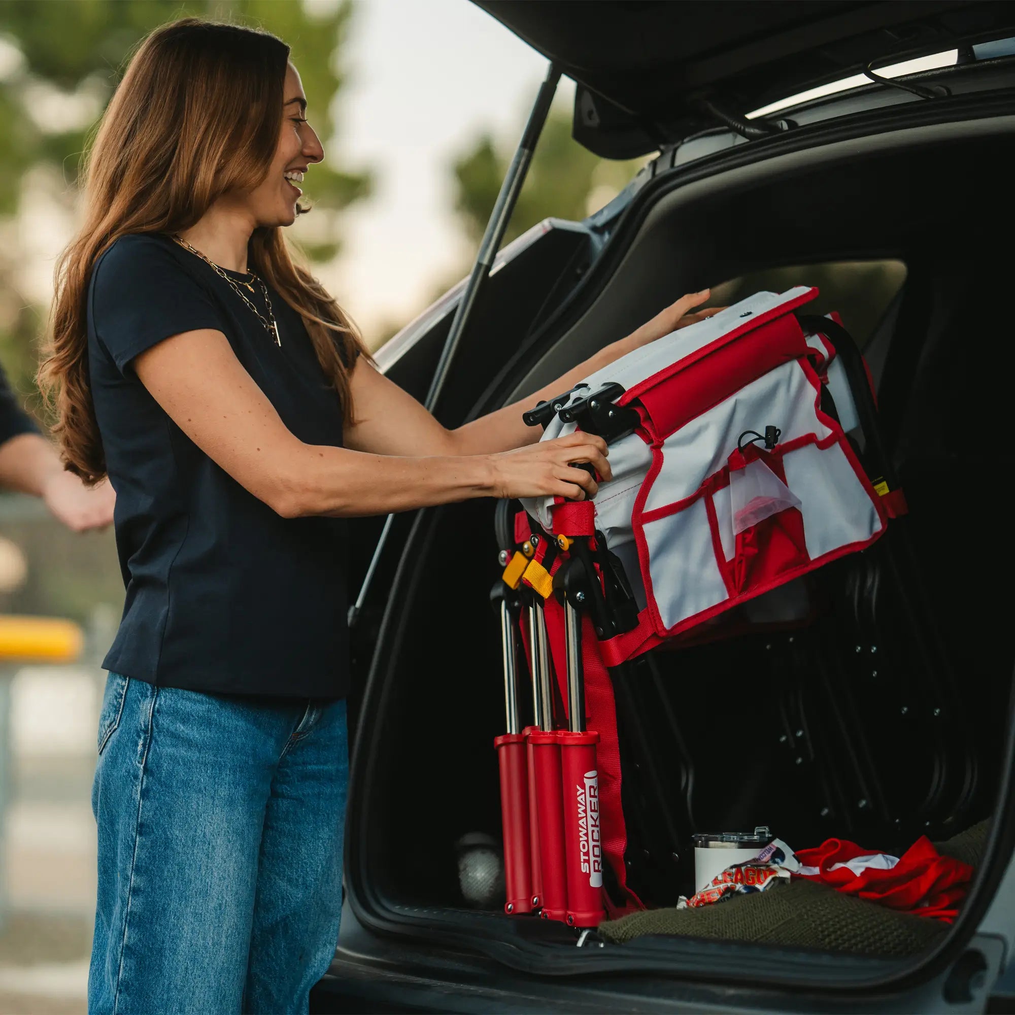 A woman loading up her folded stowaway rocker baseball print into the trunk of her car. 