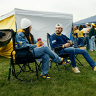 A couple sitting near a group of tailgaters while they talk in their stowaway and comfort pro rocker. 