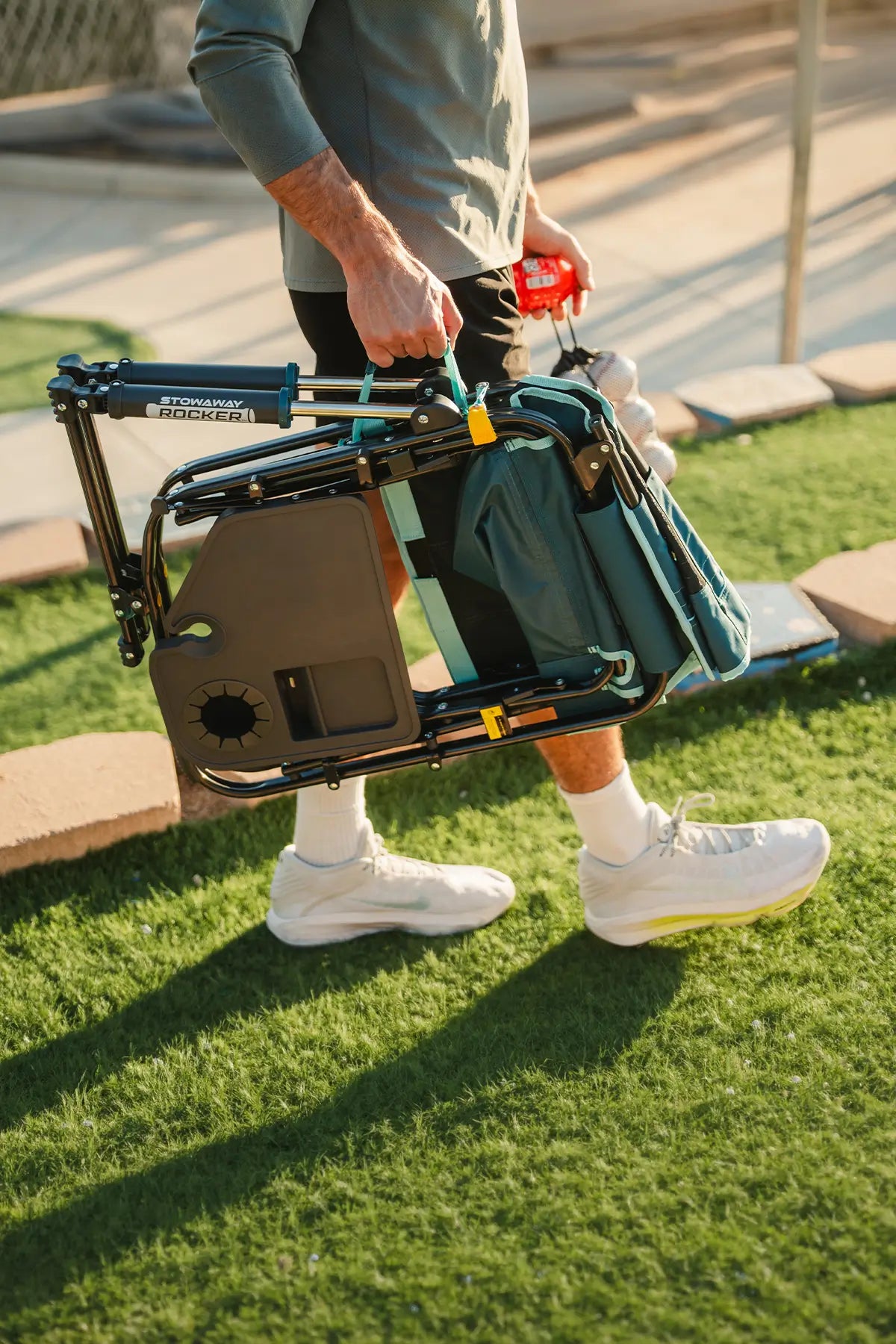 A man carrying a teal Stowaway Rocker with Side Table across a patch of grass. 