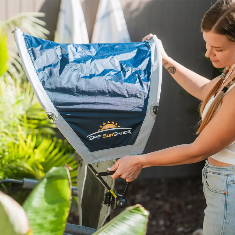 Woman adjusting the Indigo SunShade Accessory fully extended on a chair.