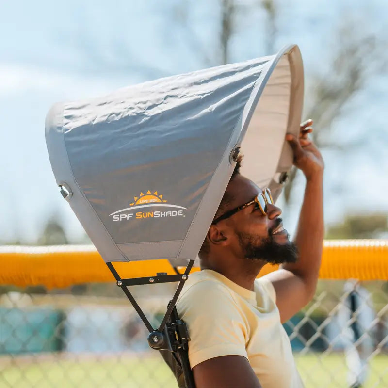 Man adjusts mercury sunshade accessory on outdoor chair during a sunny day at the ballpark.