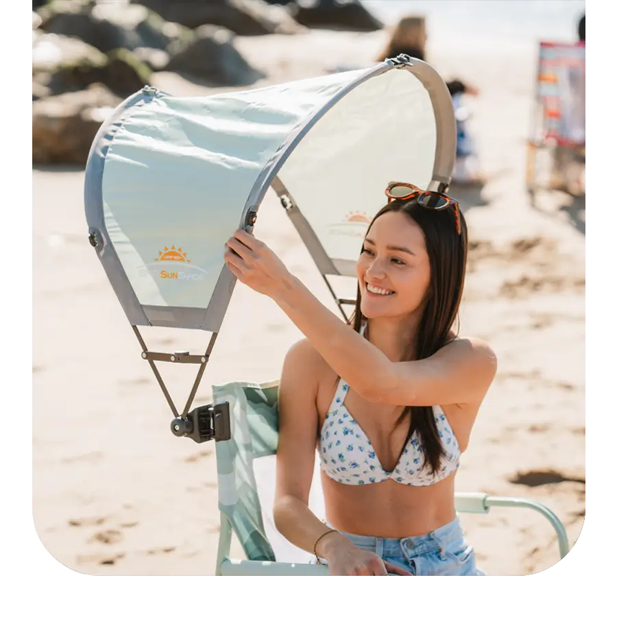 Woman adjusting a Sunshade Accessory on a beach chair while smiling in the sun.