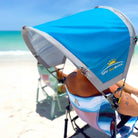 A man sitting in a beach rocker on the beach with the saybrook blue sunshade accessory attached to the chair. 