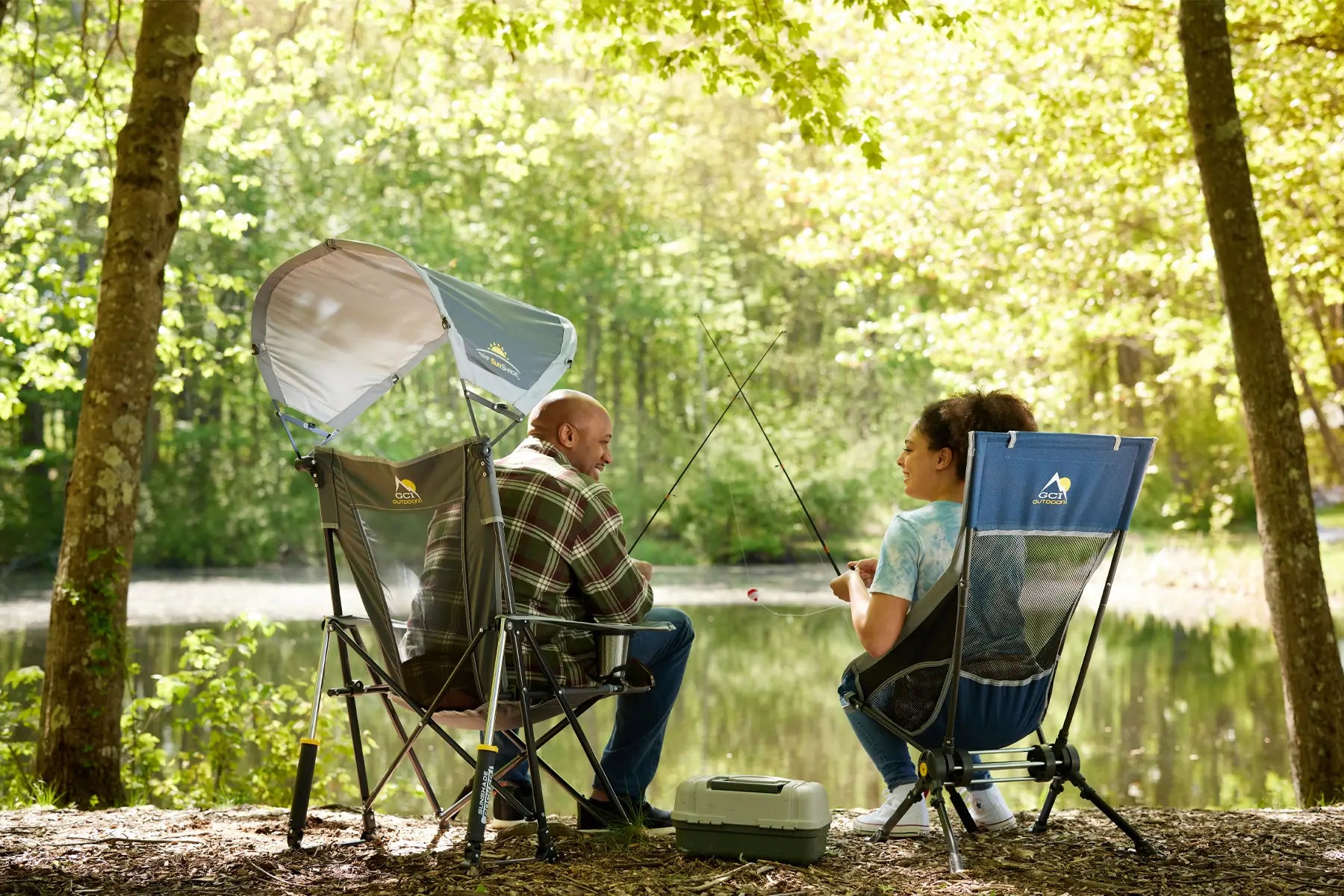 Two people fishing by a lake, one sitting in a Sunshade Rocker with the canopy open.