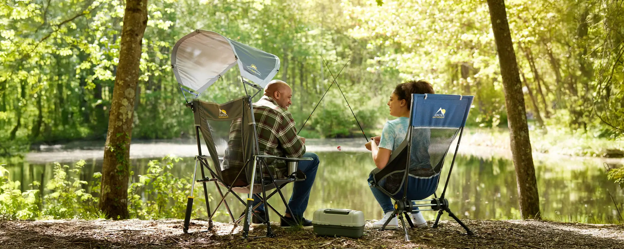 Two people fishing by a lake, one sitting in a Sunshade Rocker with the canopy open.