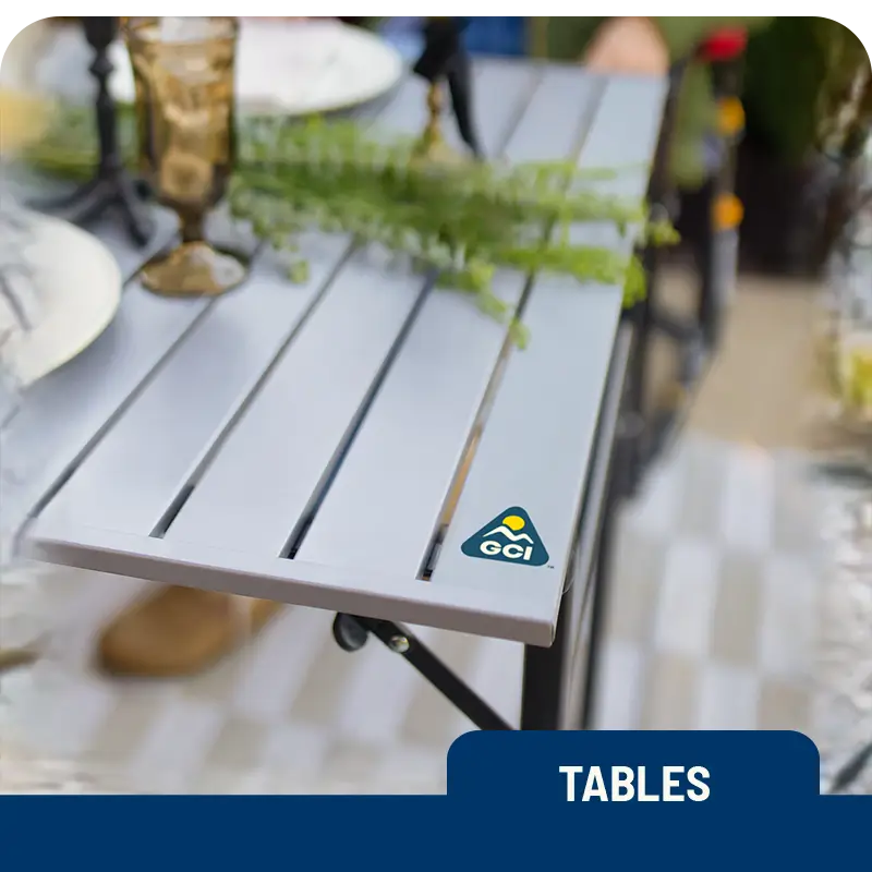 Close-up of a GCI Outdoor Slim-Fold Table with a plant centerpiece and glassware at an outdoor dining setup.