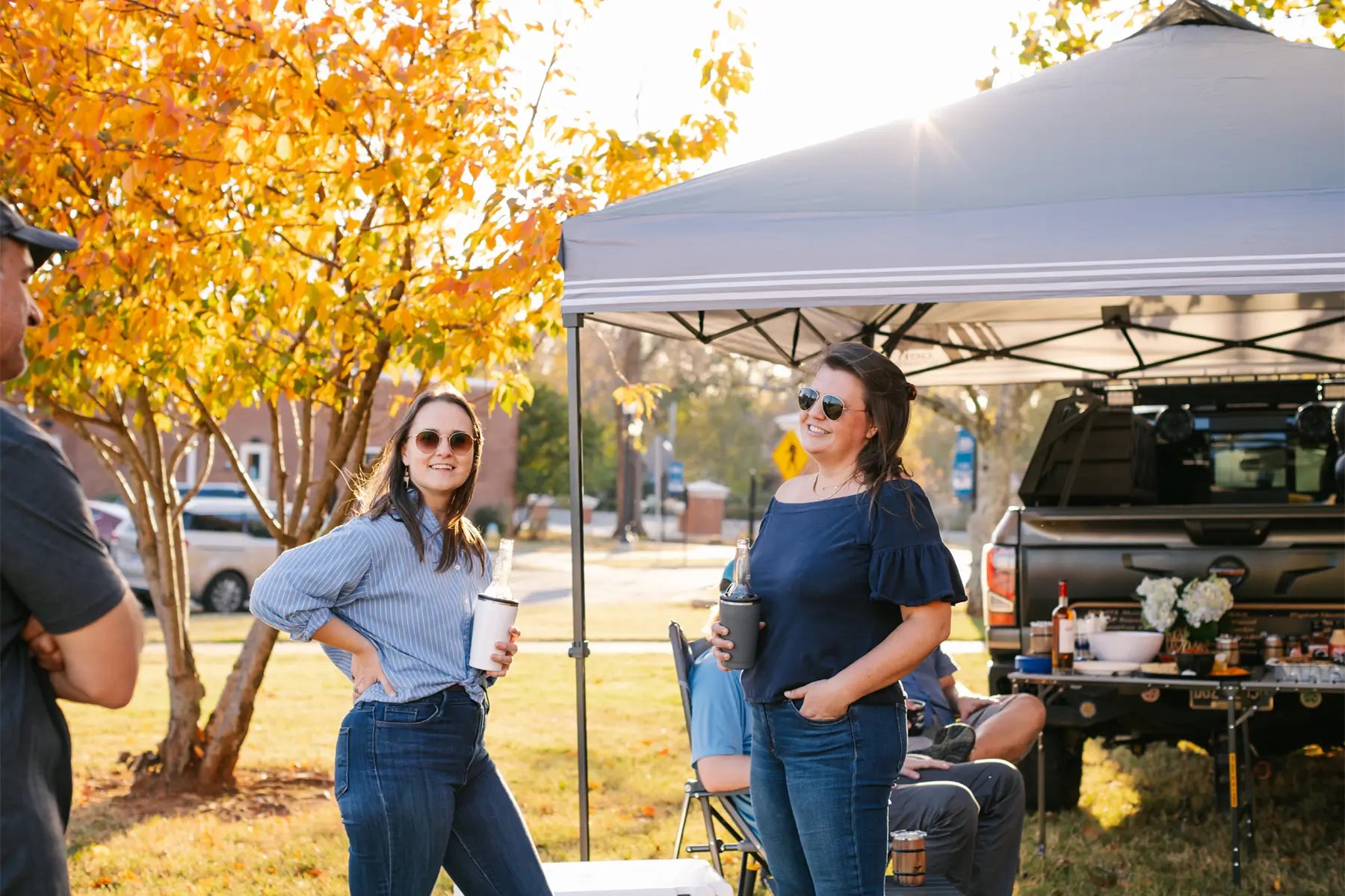 Friends hanging out under tent near a truck with food and drinks.