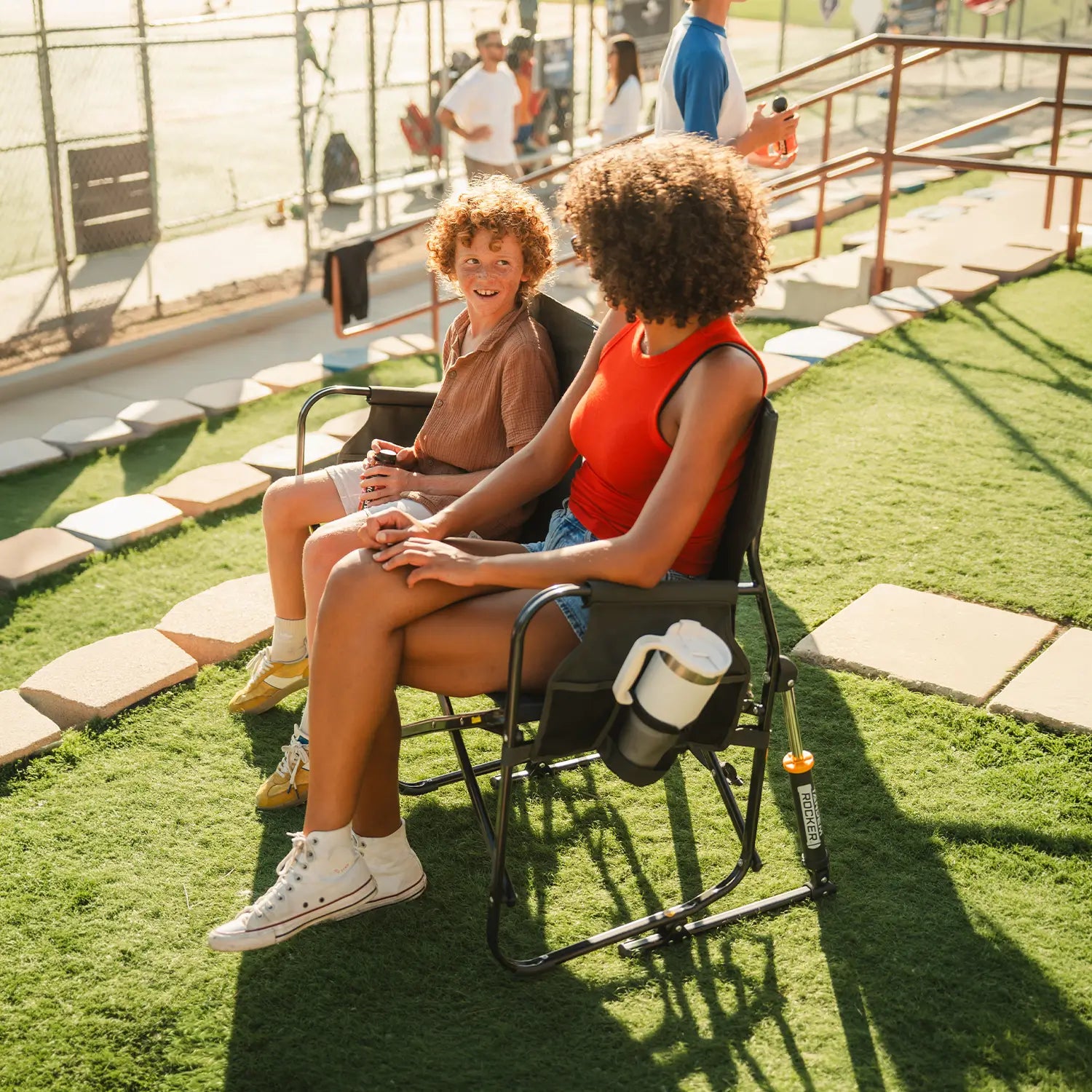 A woman sitting with a child on a Tandem Rocker while watching a baseball game. 