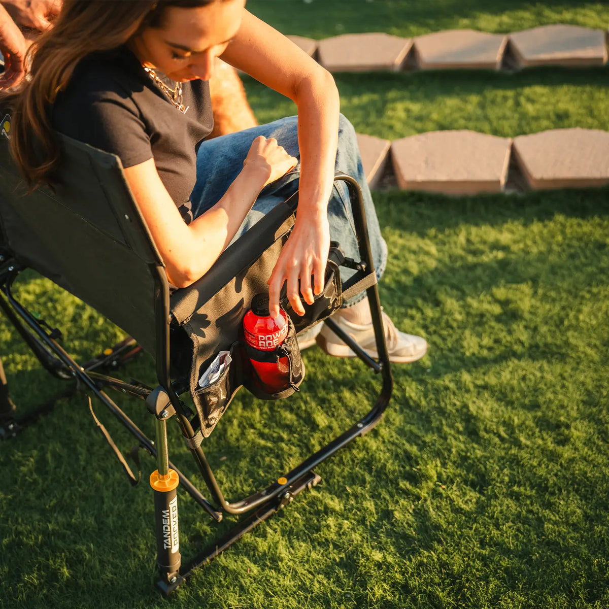 A woman reaching for a powerade drink while sitting in the Tandem Rocker at a baseball game. 