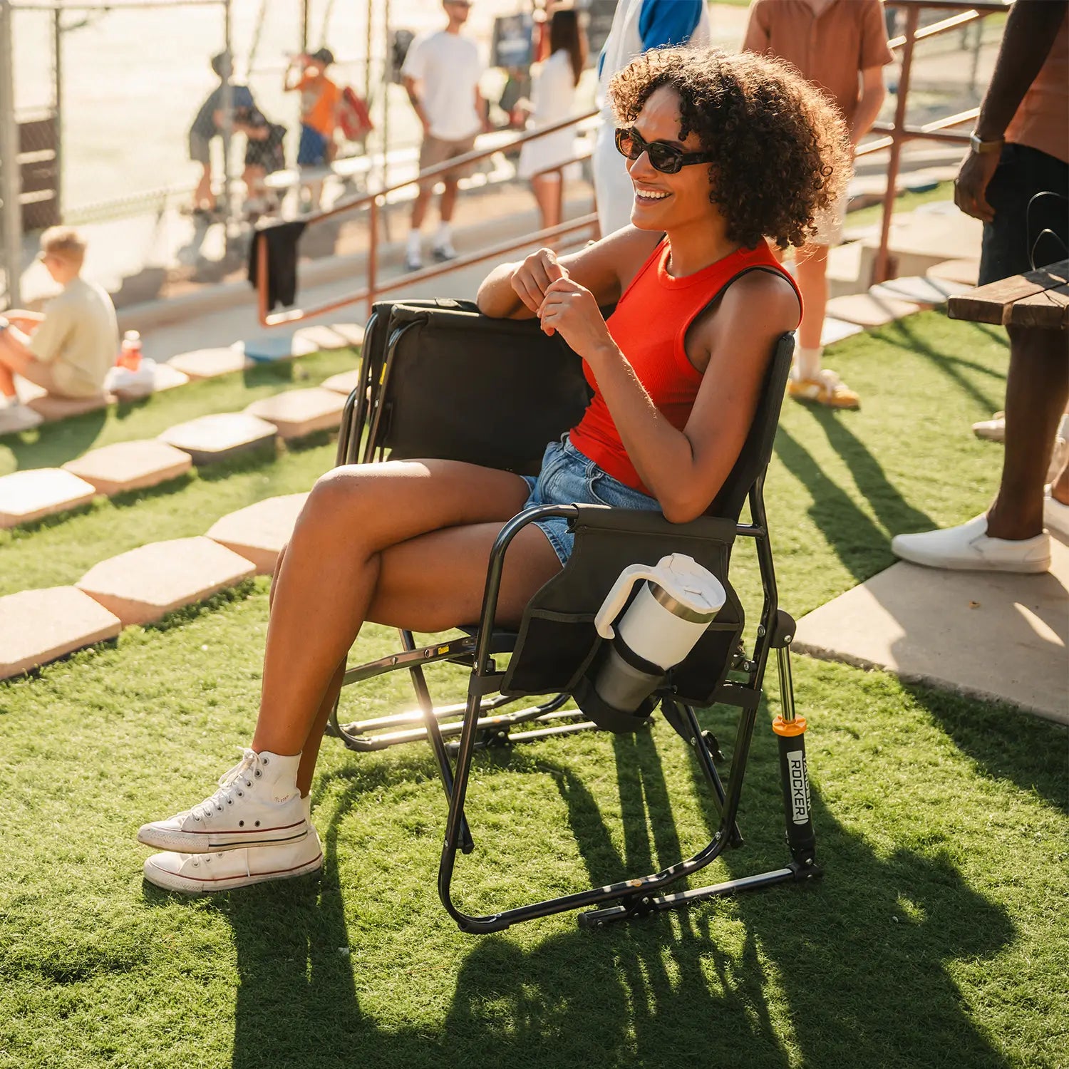 A woman sitting alone on a Tandem Rocker while watching a baseball game. 