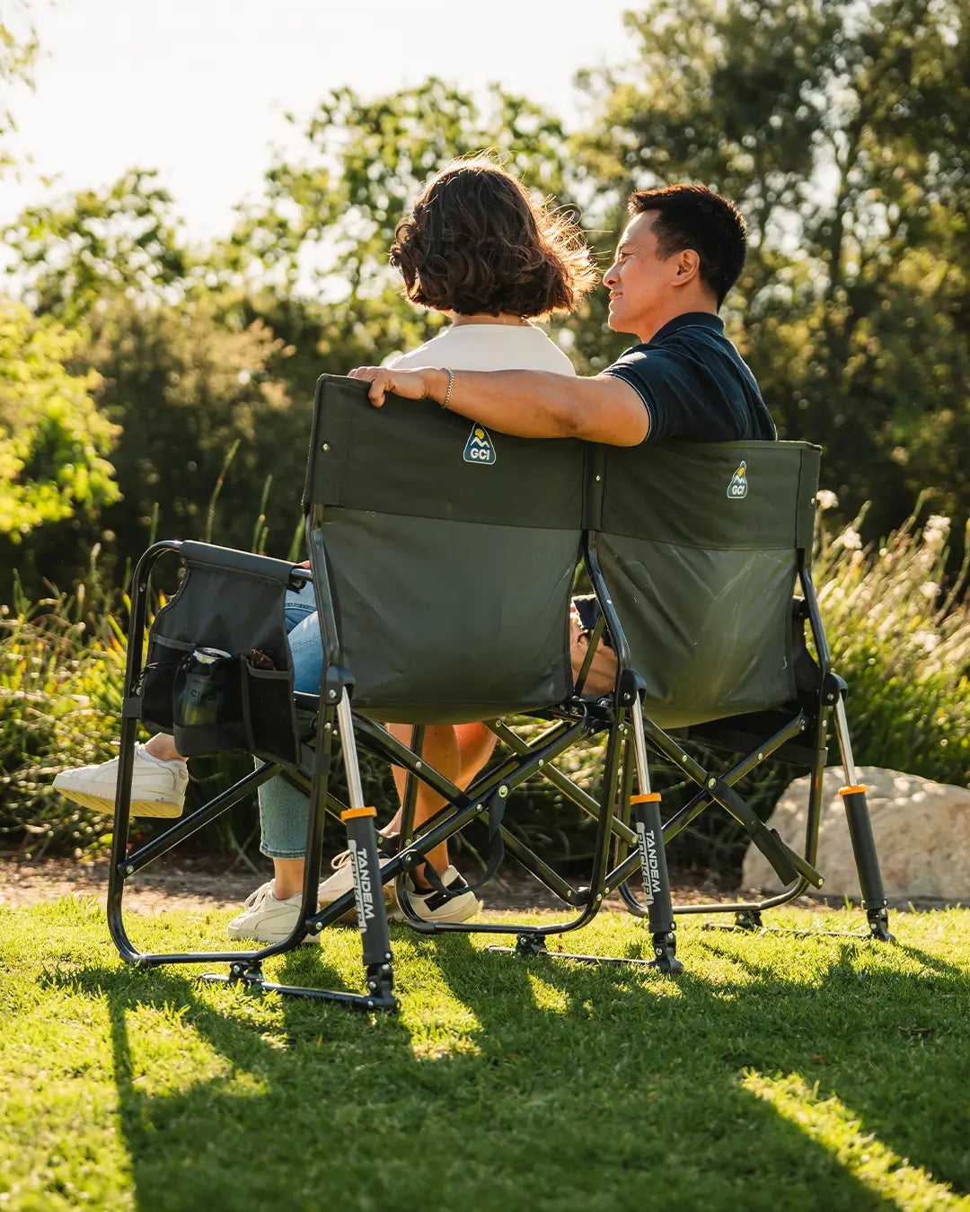 A couple sitting on a Tandem Rocker at a park. 