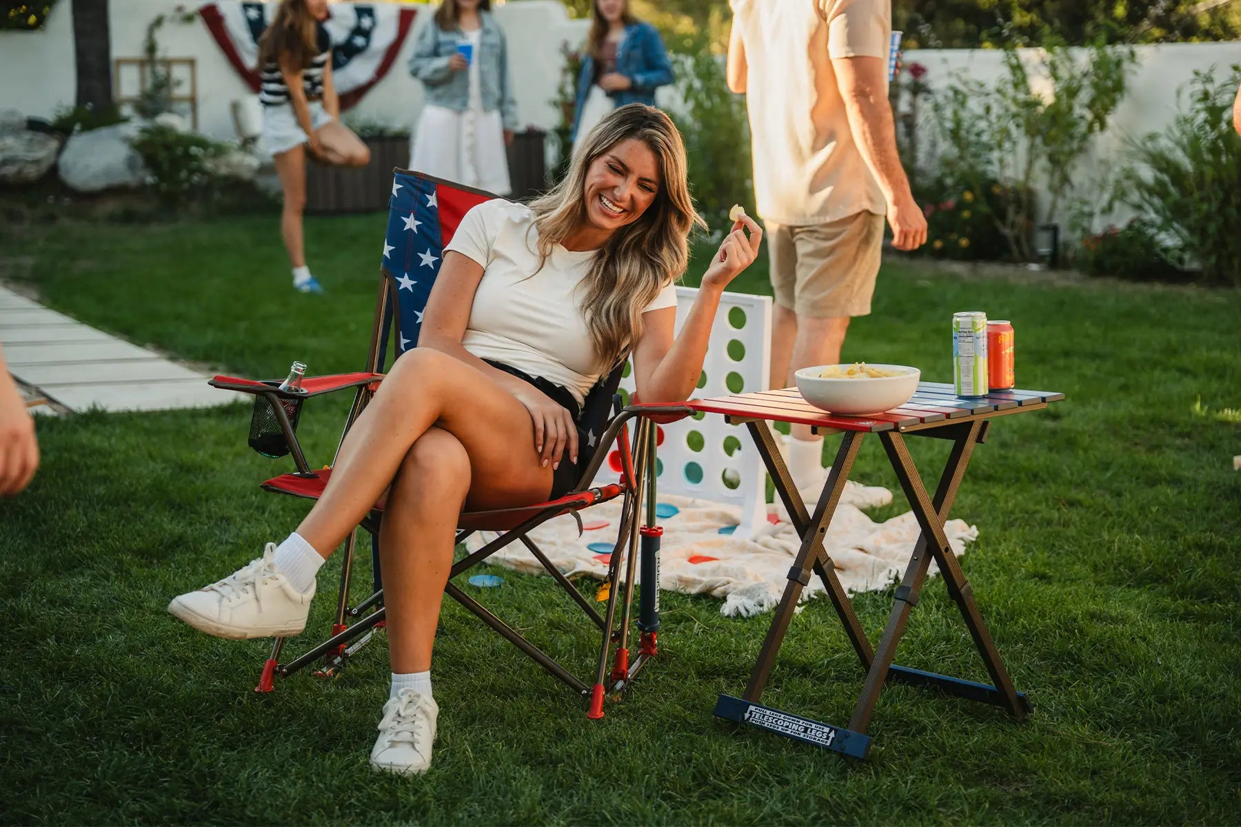A woman sitting in a USA Comfort Pro Rocker eating chips that are sitting on a USA Compact Camp Table. 