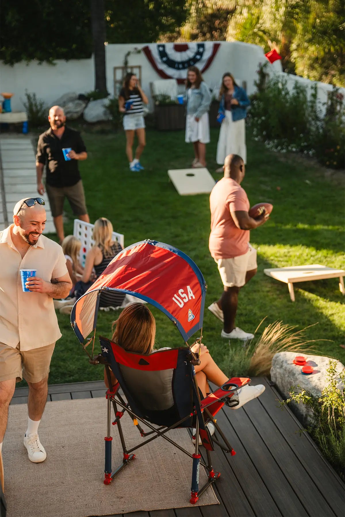 A woman sitting in a USA Comfort Pro Rocker while watching a group play football at a party. 