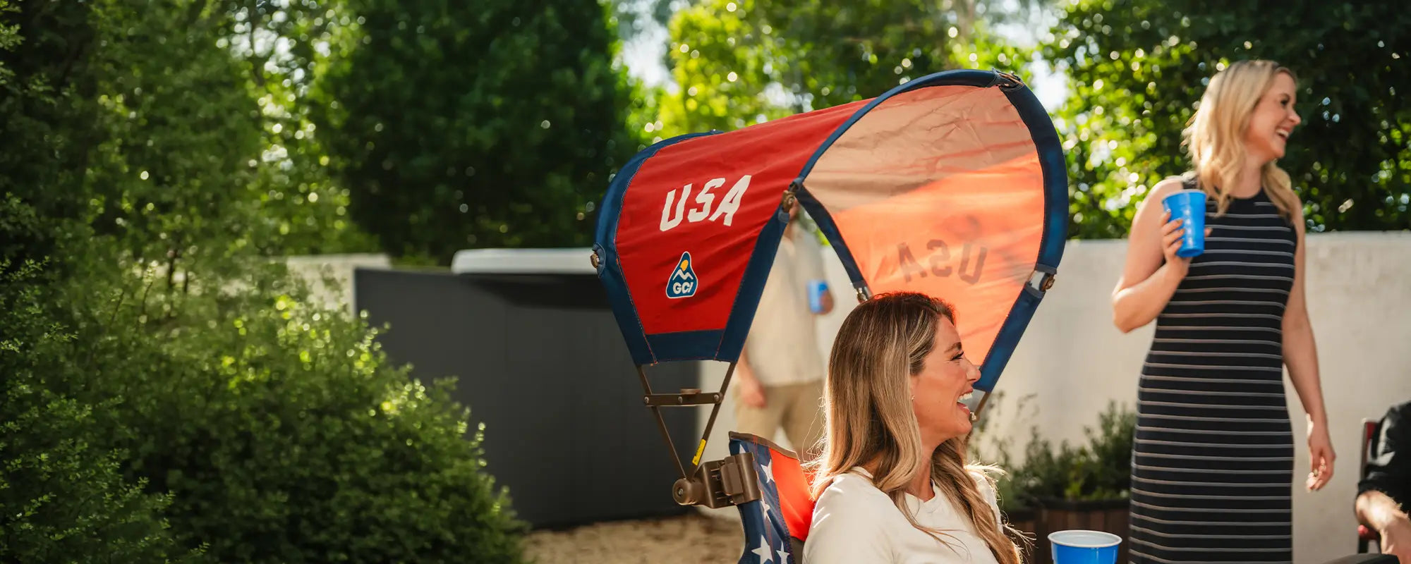 A woman smiling while sitting in a USA Comfort Pro Rocker with a USA Sunshade Accessory attached. 