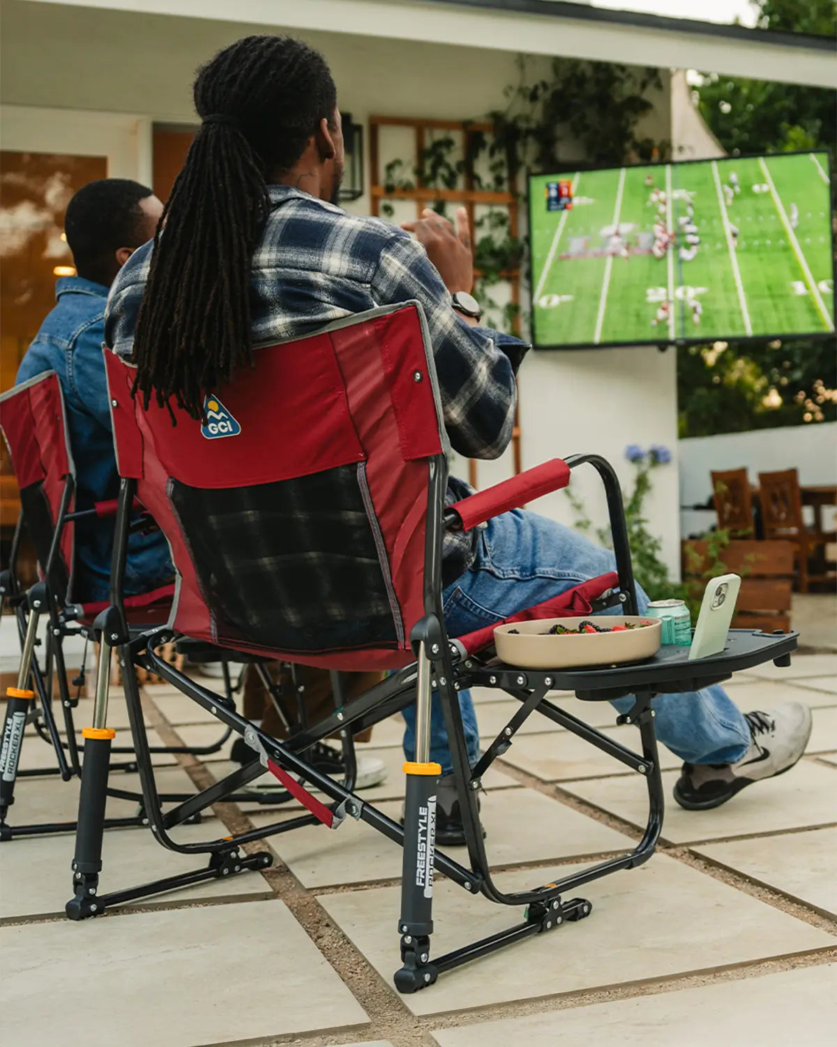 Two men watching a football game in their backyard while sitting in freestyle xl rockers with side tables. 