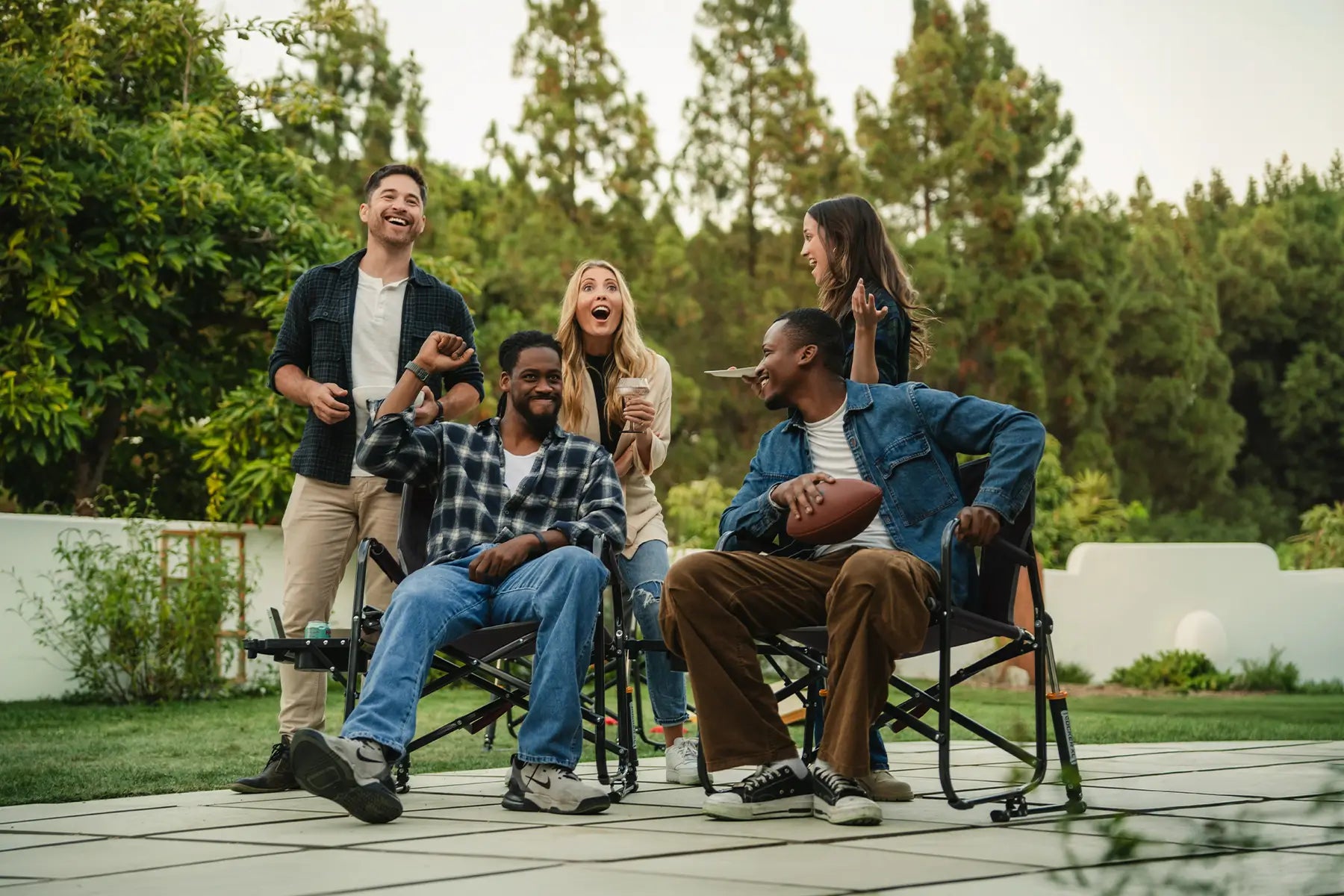 A group of people gathered watching a football game while two men sit in Freestyle Rocker chairs. 