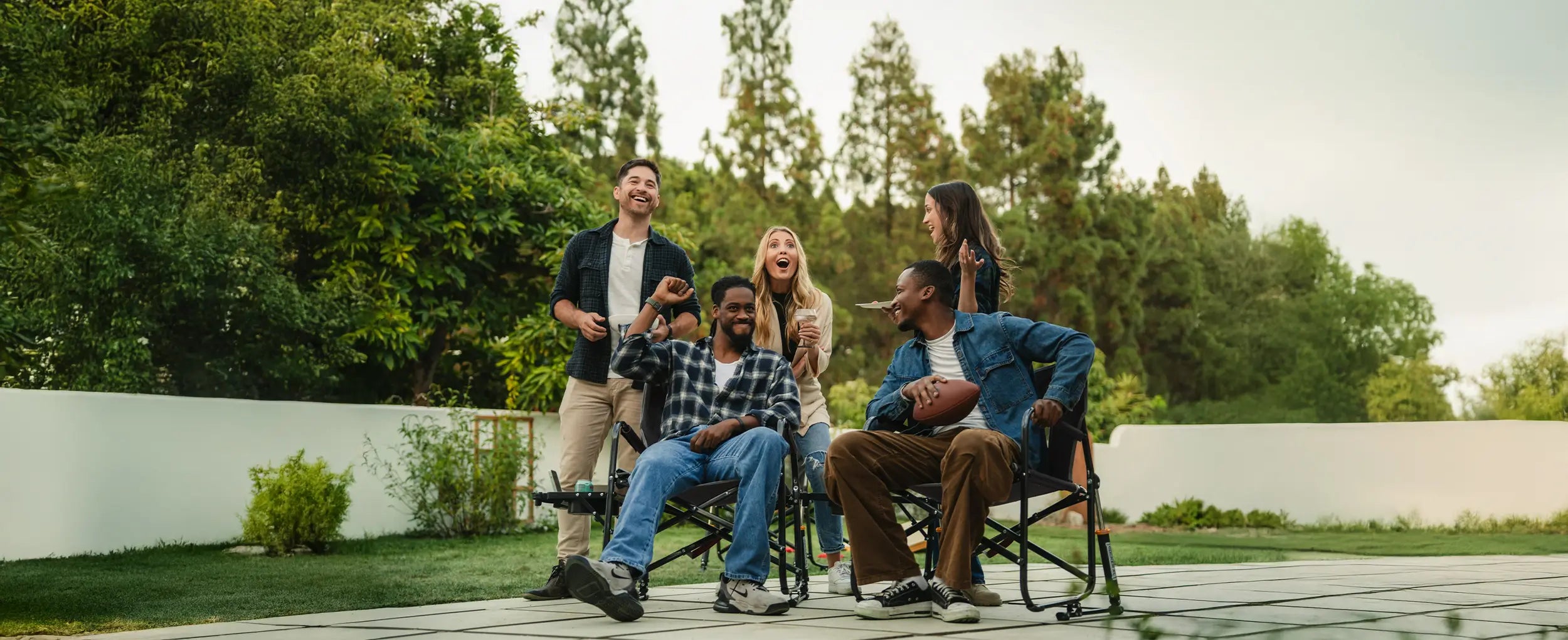 A group of people gathered watching a football game while two men sit in Freestyle Rocker chairs. 