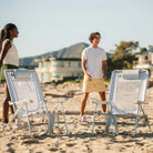 Two GCI Big Surf chairs with Slide Table in light blue mosaic on the sand, with a man and woman standing near them.