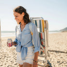 Front view of a woman carrying a GCI Big Surf chair with Slide Table in retro beach stripes backpack-style, holding a canned drink.