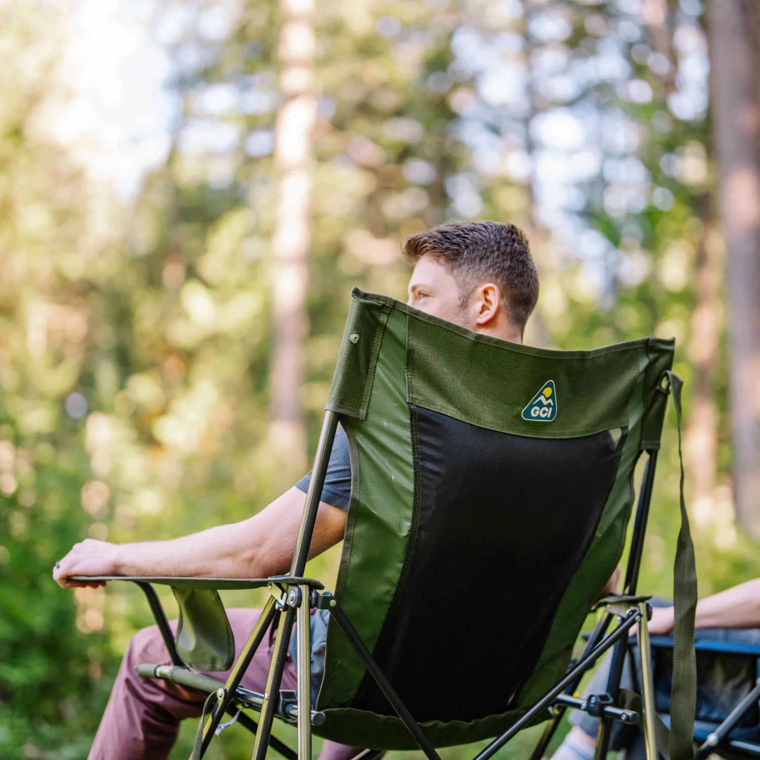 Back view of a man seated in a heathered olive Comfort Pro Rocker XL, with GCI logo visible on the backrest.