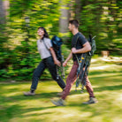 Man and woman walk through a grassy, wooded area each carrying a folded Comfort Pro Rocker XL over their shoulder.