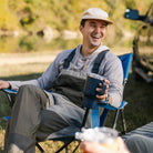 A man smiling while holding a cup and sitting in a blue Comfort Quad chair. 