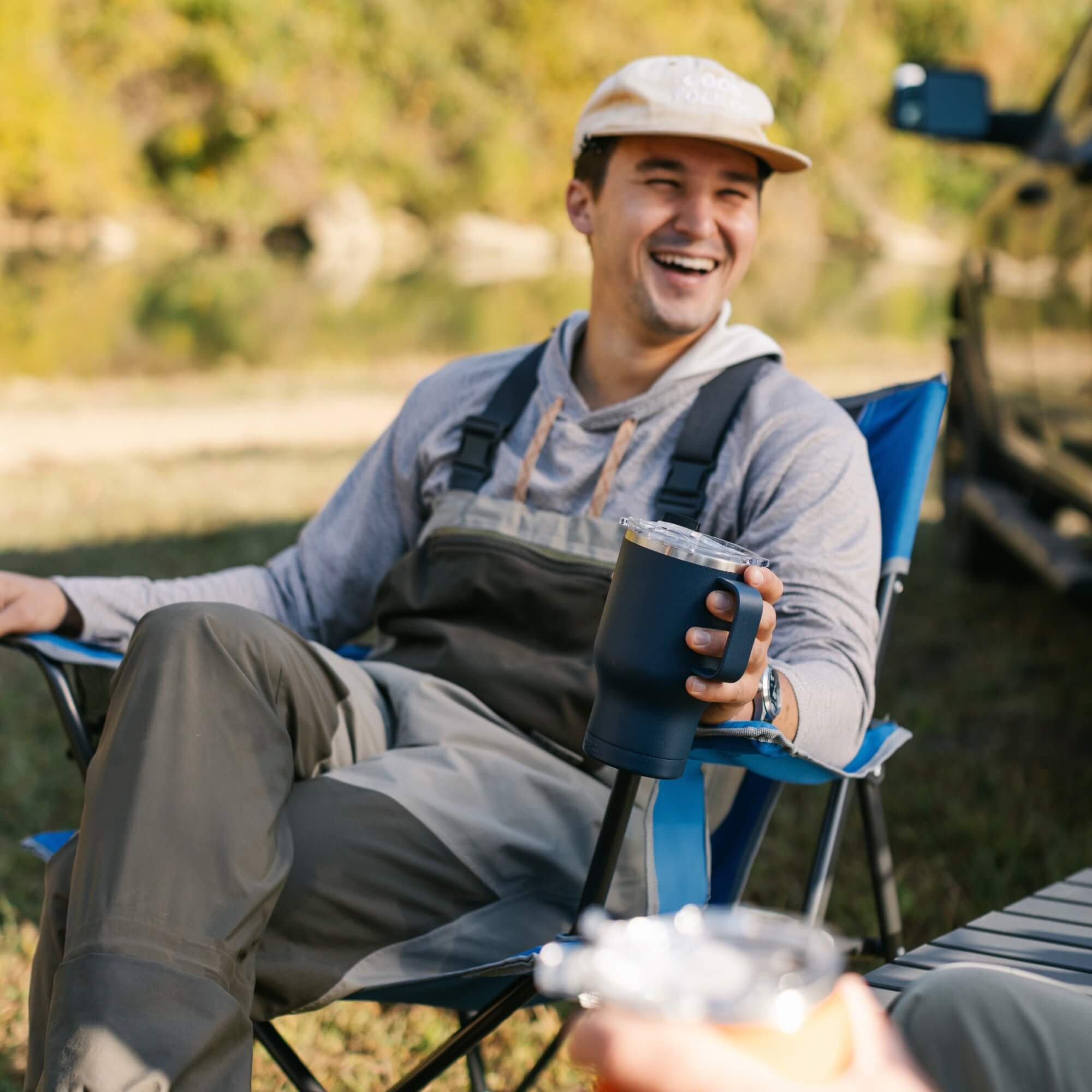 A man smiling while holding a cup and sitting in a blue Comfort Quad chair. 