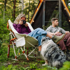 Woman photographs a dog while relaxing in a natural Fleece Rocker with her feet up, near a cabin in the woods.