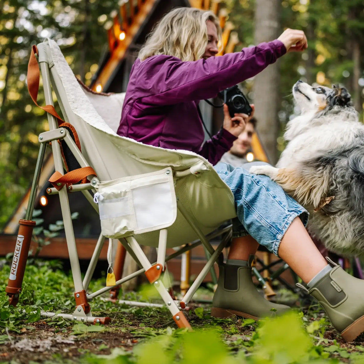 Woman leans out of a natural Fleece Rocker to give the dog beside her a treat.