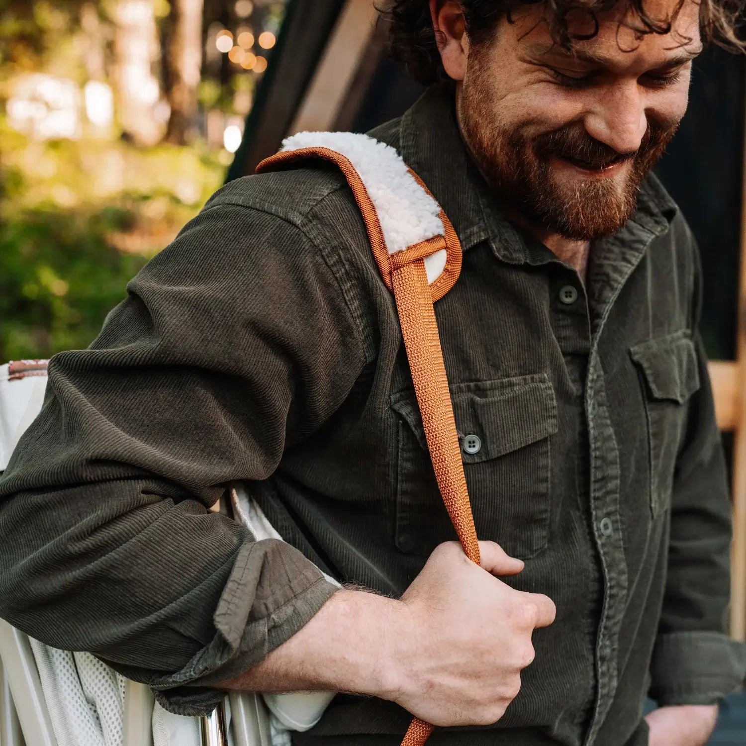 Close-up of a man carrying a folded natural Fleece Rocker by the shoulder strap.