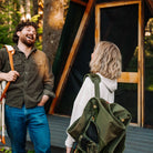 Woman carries a folded olive Fleece Rocker over her shoulder while talking with a man outside a cabin.